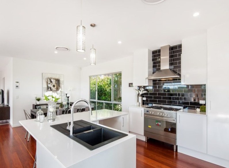 White kitchen with island bench, black splashback, pendant lights and downlights