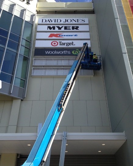 Boom lift raised to shopping centre signage for David Jones, Myer, Kmart, Target and Woolworths